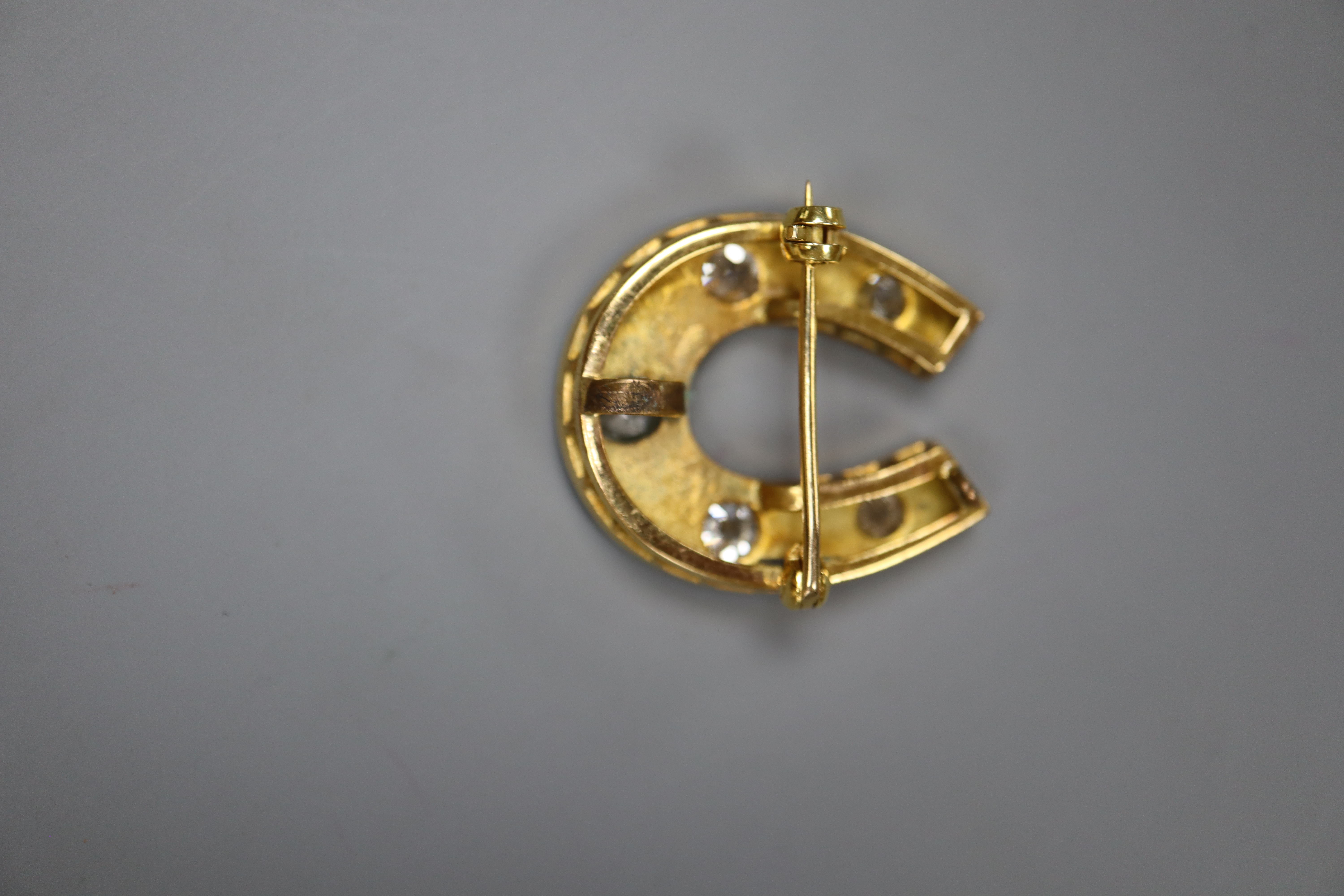 A yellow metal and five stone round cut diamond set horseshoe pendant brooch, 26mm, gross 8.8 grams.